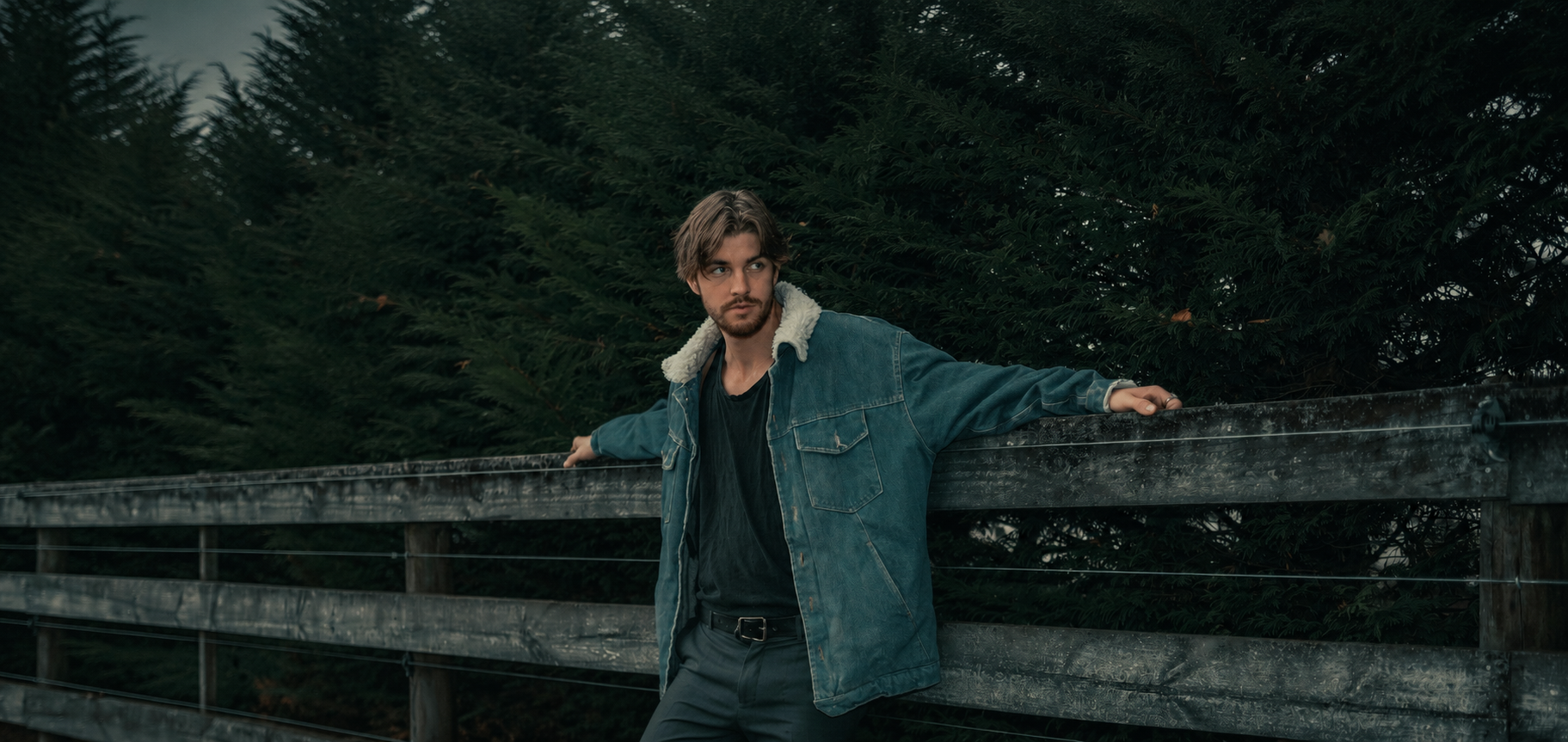 Man standing on a wooden bridge with a forest background wearing denim jaket