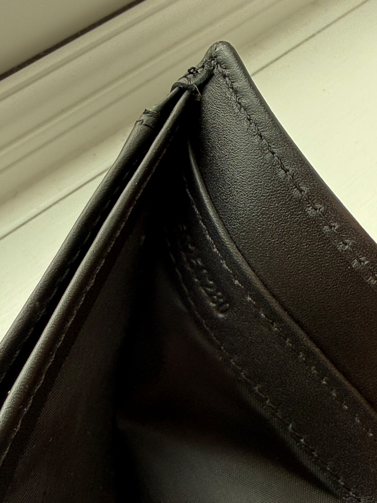 Close-up of a black leather wallet with visible stitching on a light wooden surface.
