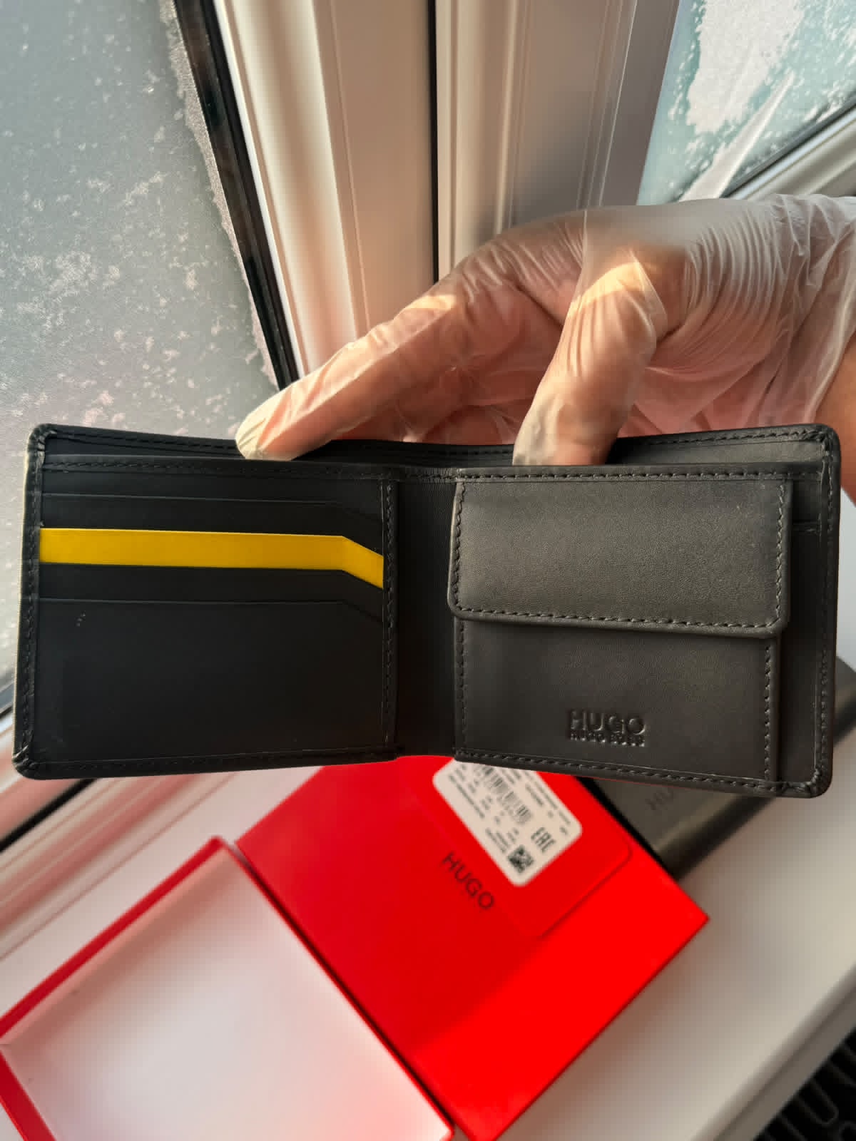 Black wallet with yellow stripe held by a gloved hand, with a red box in the background